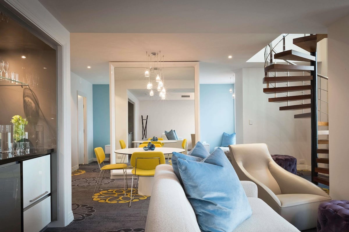 A modern living room with a sofa, a dining area with yellow chairs, and a staircase.