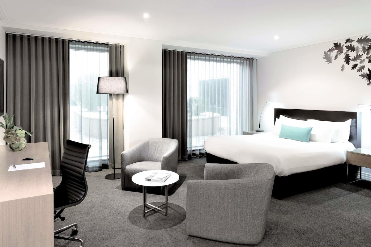 A modern hotel room with a large bed, two armchairs, a small table, and a desk.