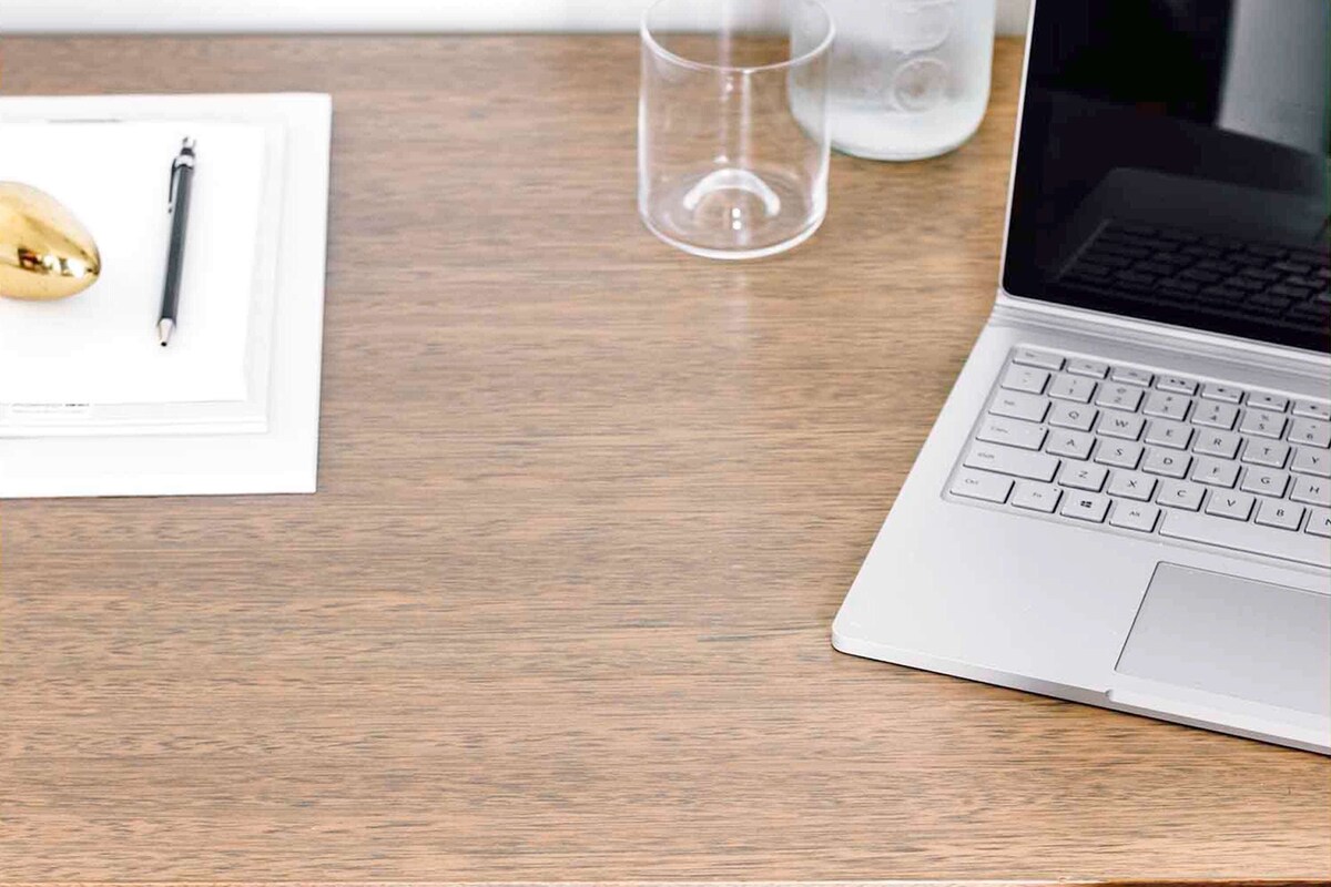 A laptop on a wooden desk with a pen, a mouse, and a glass of water.