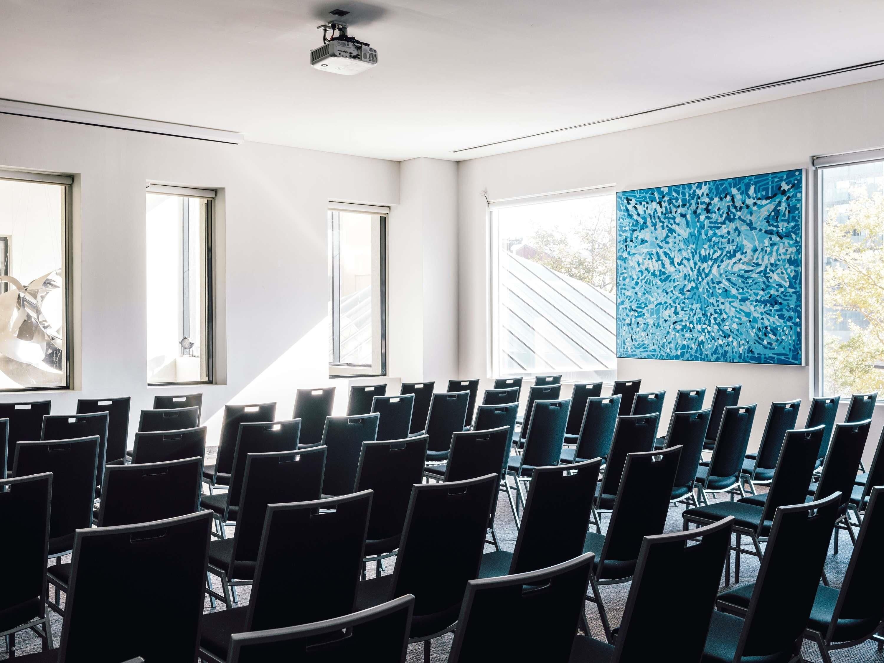 A conference room with rows of chairs, large windows, and a projector on the ceiling.