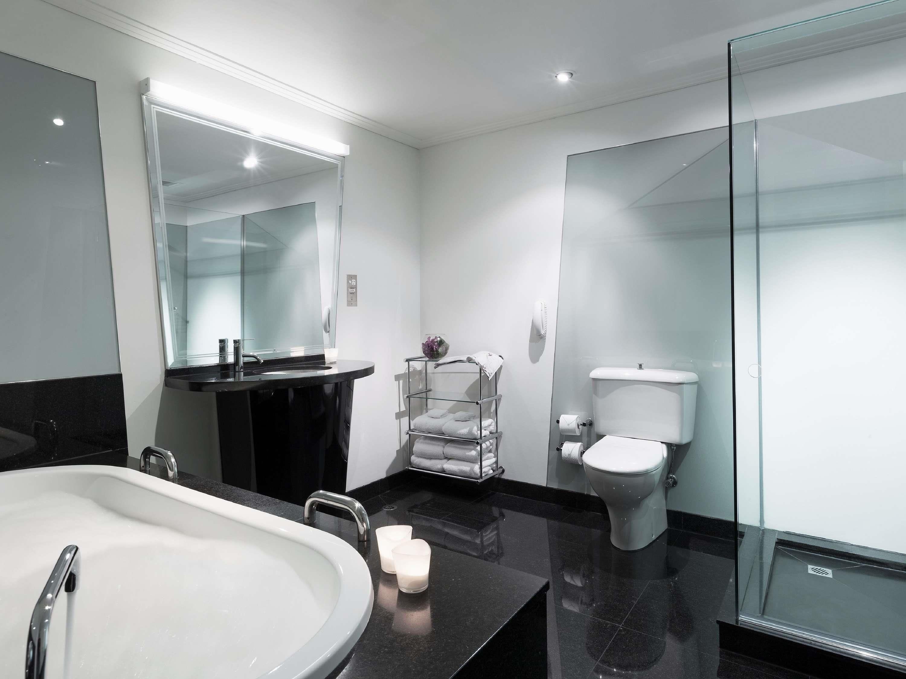 A modern bathroom with a large white bathtub, a black vanity with a mirror, a glass shower enclosure, and a toilet.