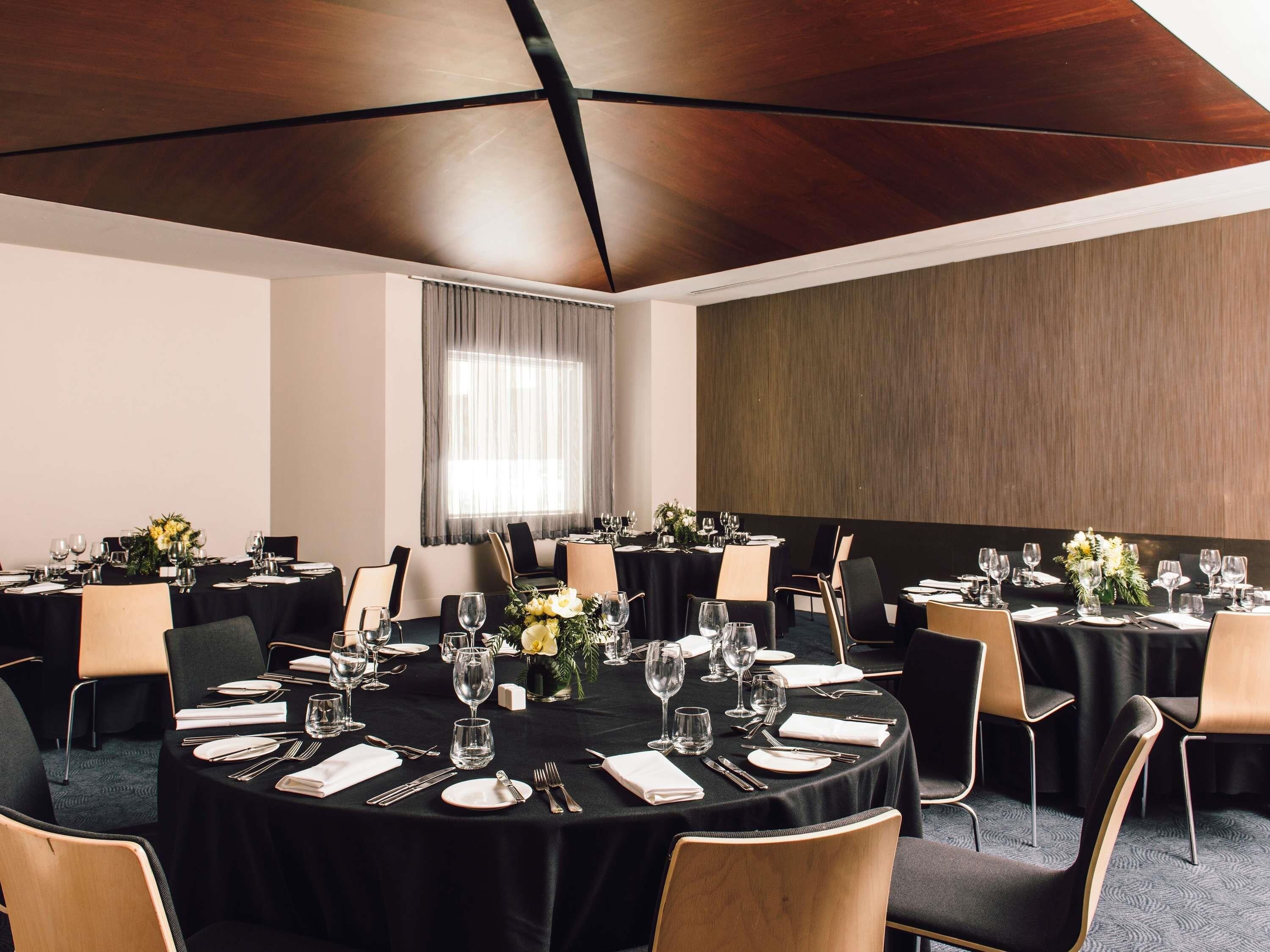 Un salón de conferencias con mesas redondas, manteles negros y sillas.