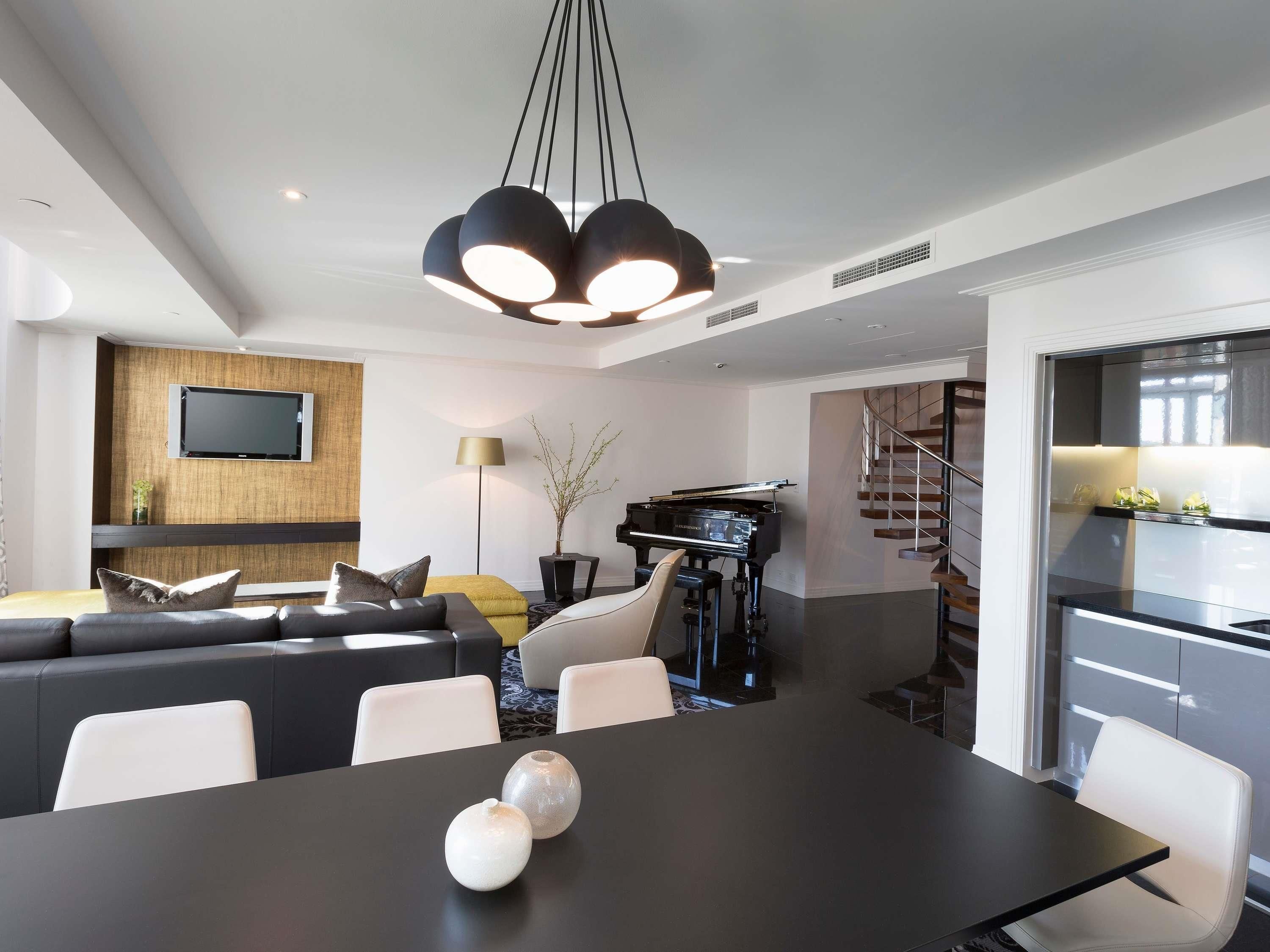 Un salon moderne avec une table à manger noire, un ensemble de canapés, un piano et un téléviseur fixé au mur.