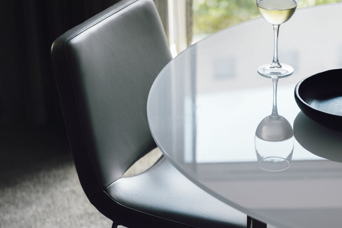 A modern dining area with a round table, a glass wine glass, and a black bowl.