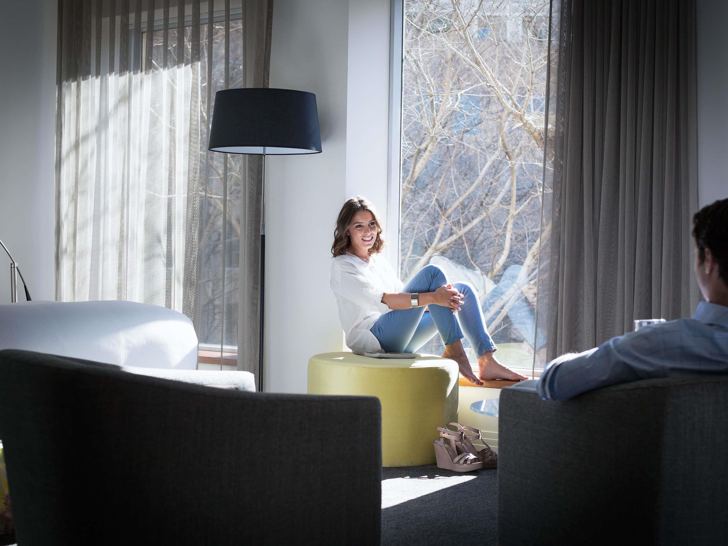 A hotel room with a bed, a sofa, a floor lamp, and a window with a view of trees.