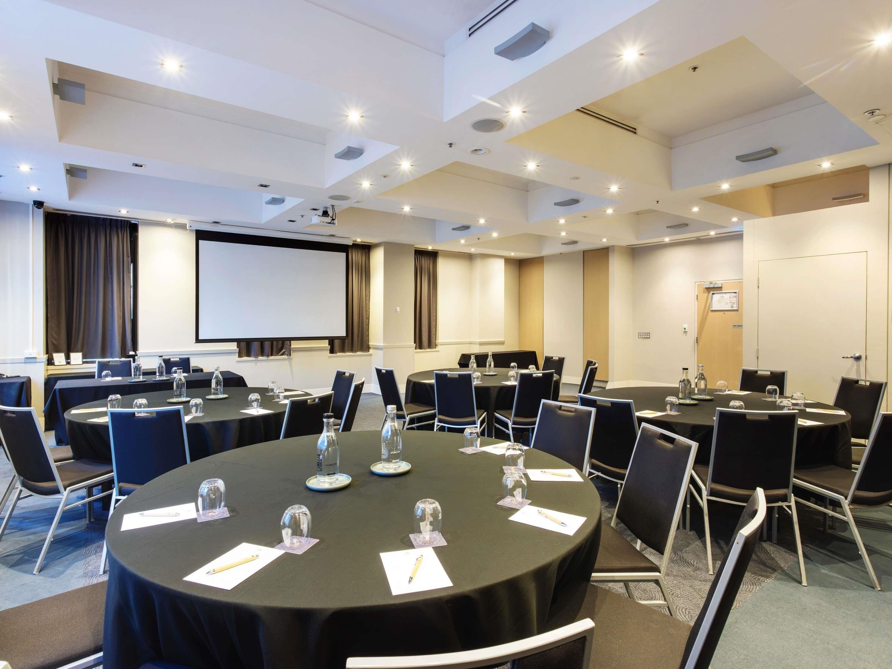 A conference room with multiple tables, chairs, and a projector screen.