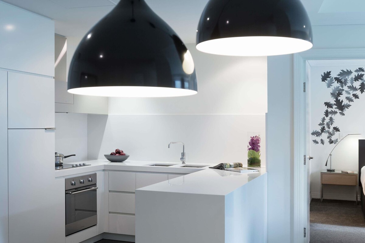 A modern kitchen with white cabinetry, a built-in oven, a sink, and two pendant lights.