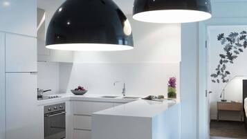 Una cocina moderna con armarios blancos, horno empotrado, fregadero y dos lámparas colgantes.