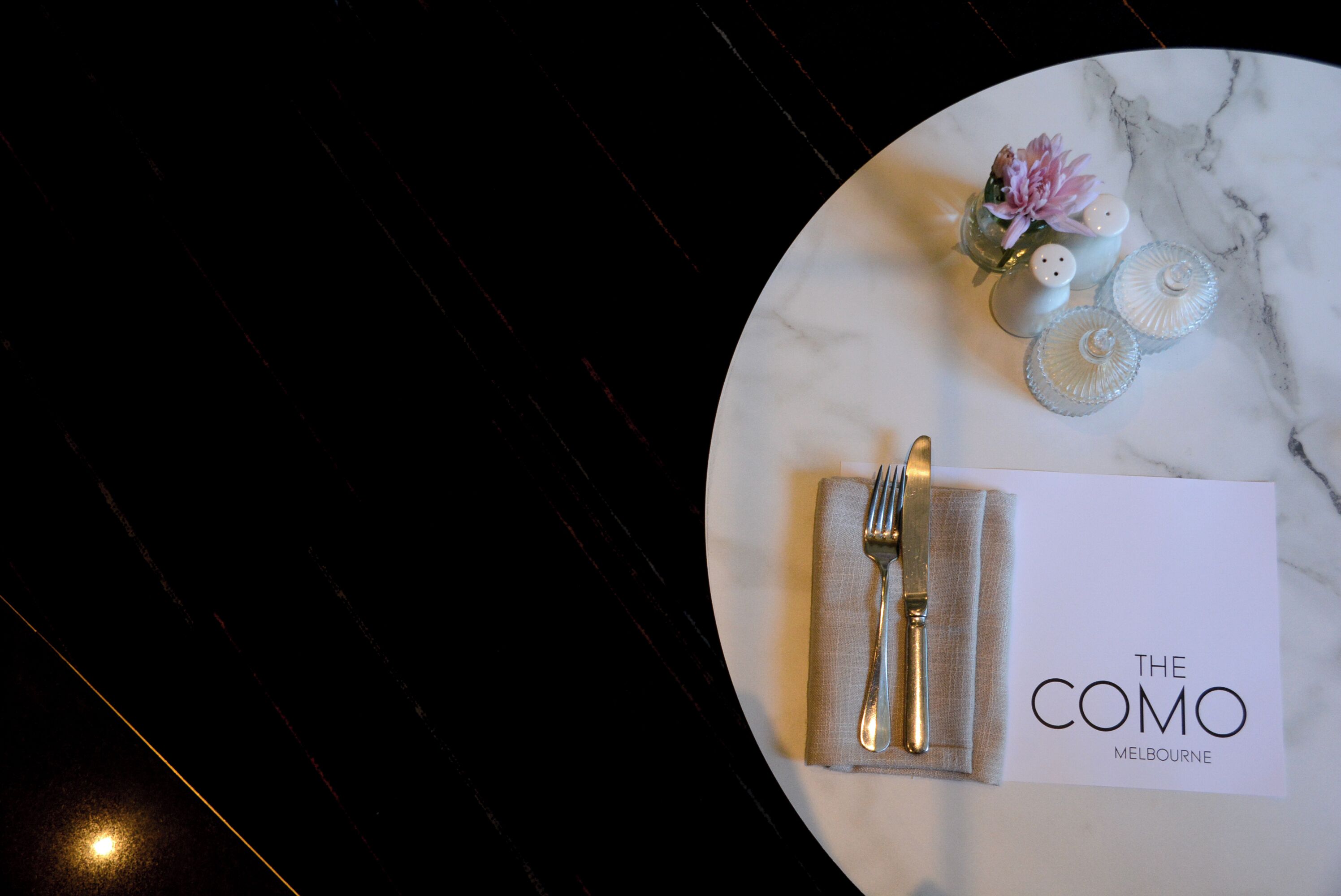 A table set with a folded napkin, cutlery, and a card reading "THE COMO MELBOURNE".