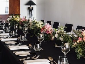 Uma longa mesa posta para um evento formal, com diversos lugares, copos e arranjos florais.