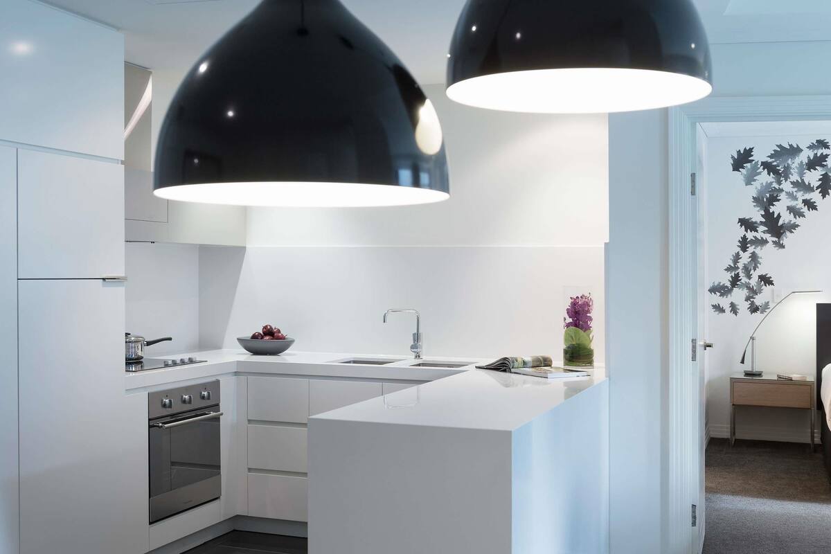 A modern kitchen with white cabinetry, a built-in oven, a sink, and two pendant lights.