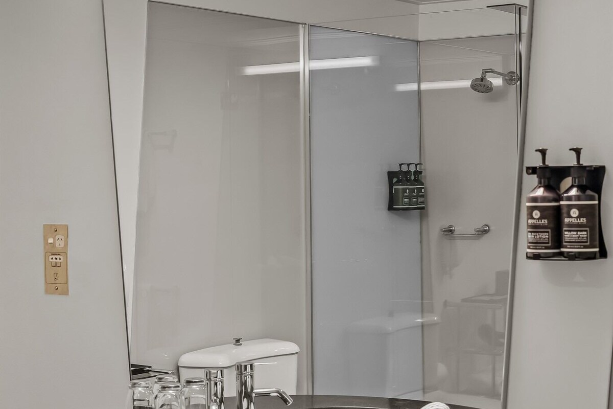 A bathroom with a large mirror, a sink, a shower, and a towel rack.