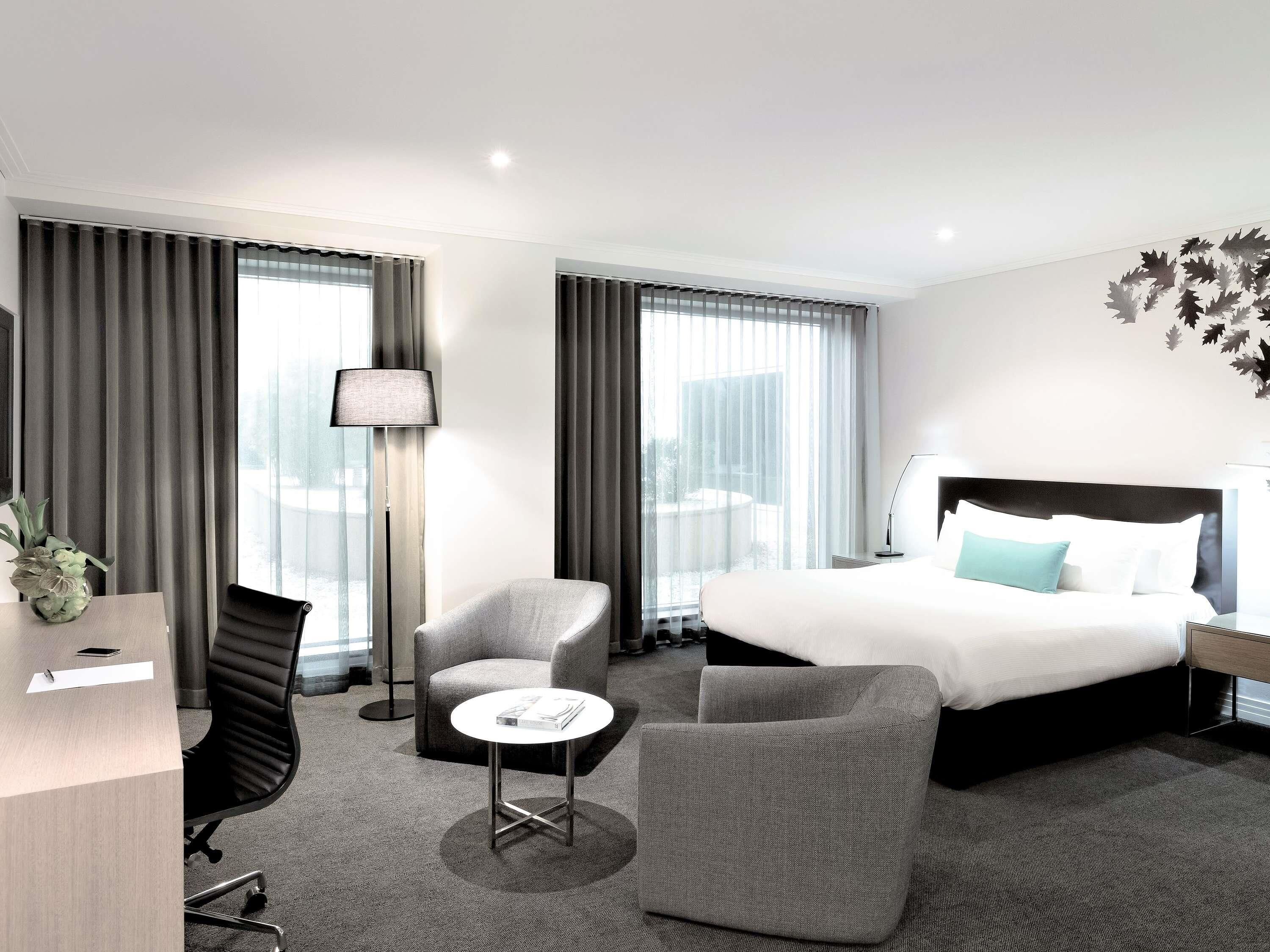 A modern hotel room with a large bed, two armchairs, a small table, and a desk.