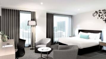 A modern hotel room with a large bed, two armchairs, a small table, and a desk.