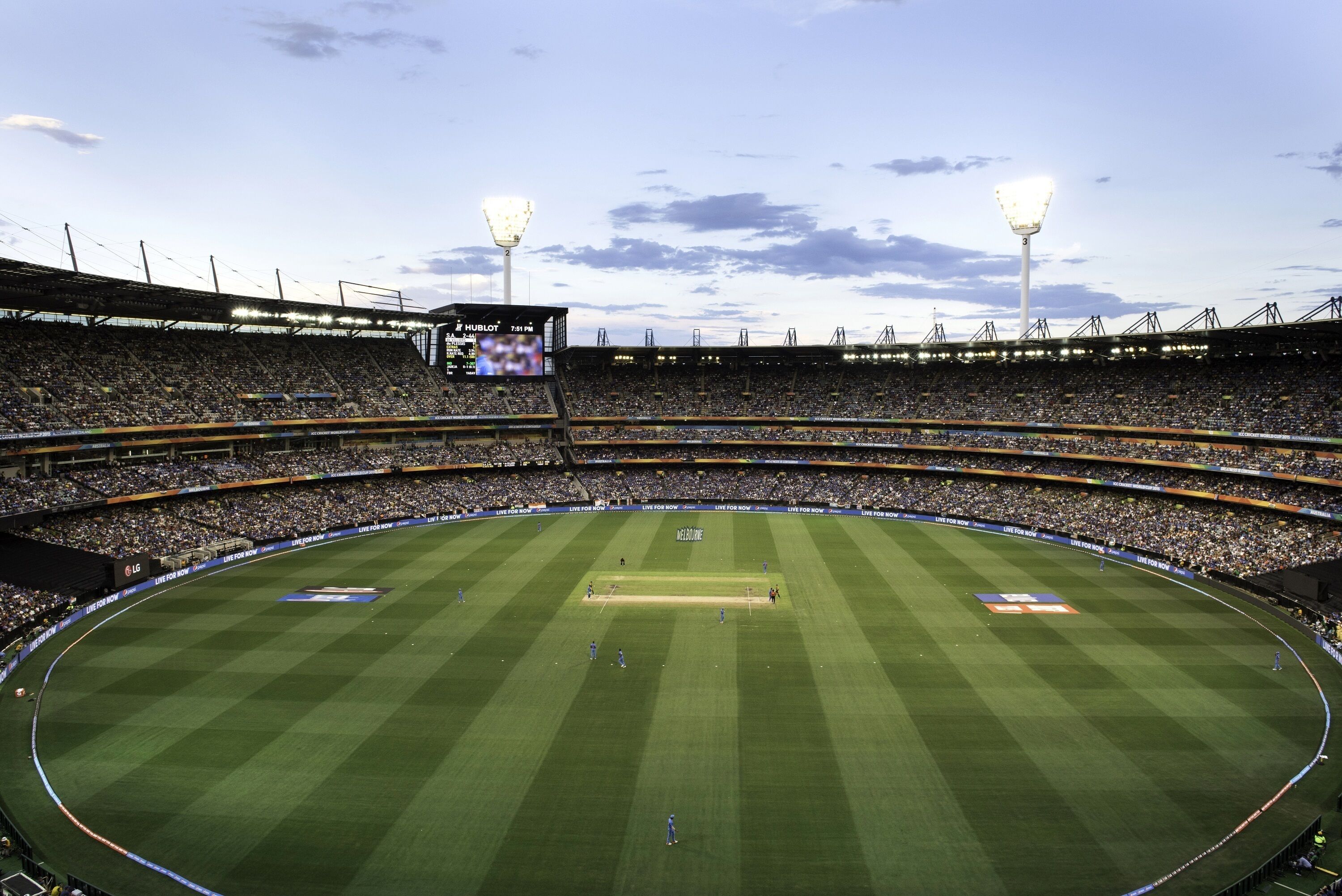 A large stadium with multiple tiers of seating, a scoreboard, and floodlights.
