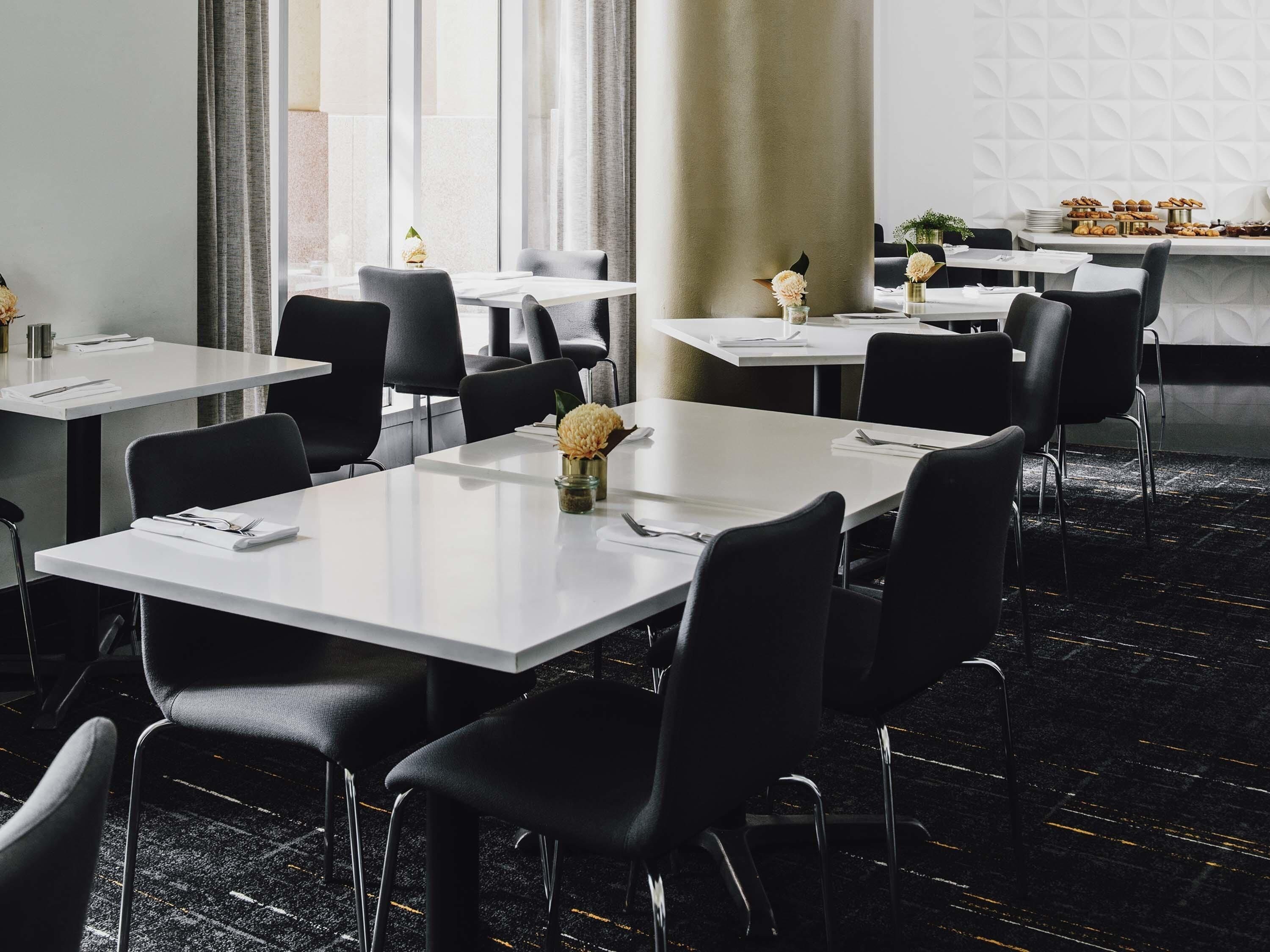 A modern dining area with white tables, black chairs, and a carpeted floor.