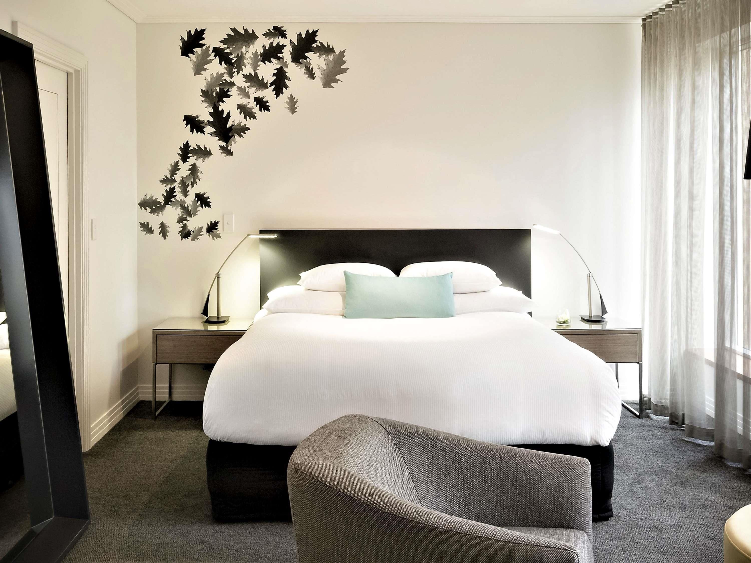 A hotel room with a large bed, two bedside tables, a chair, and a wall decal.