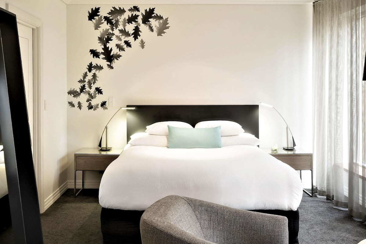 A hotel room with a large bed, two bedside tables, a chair, and a wall decal.