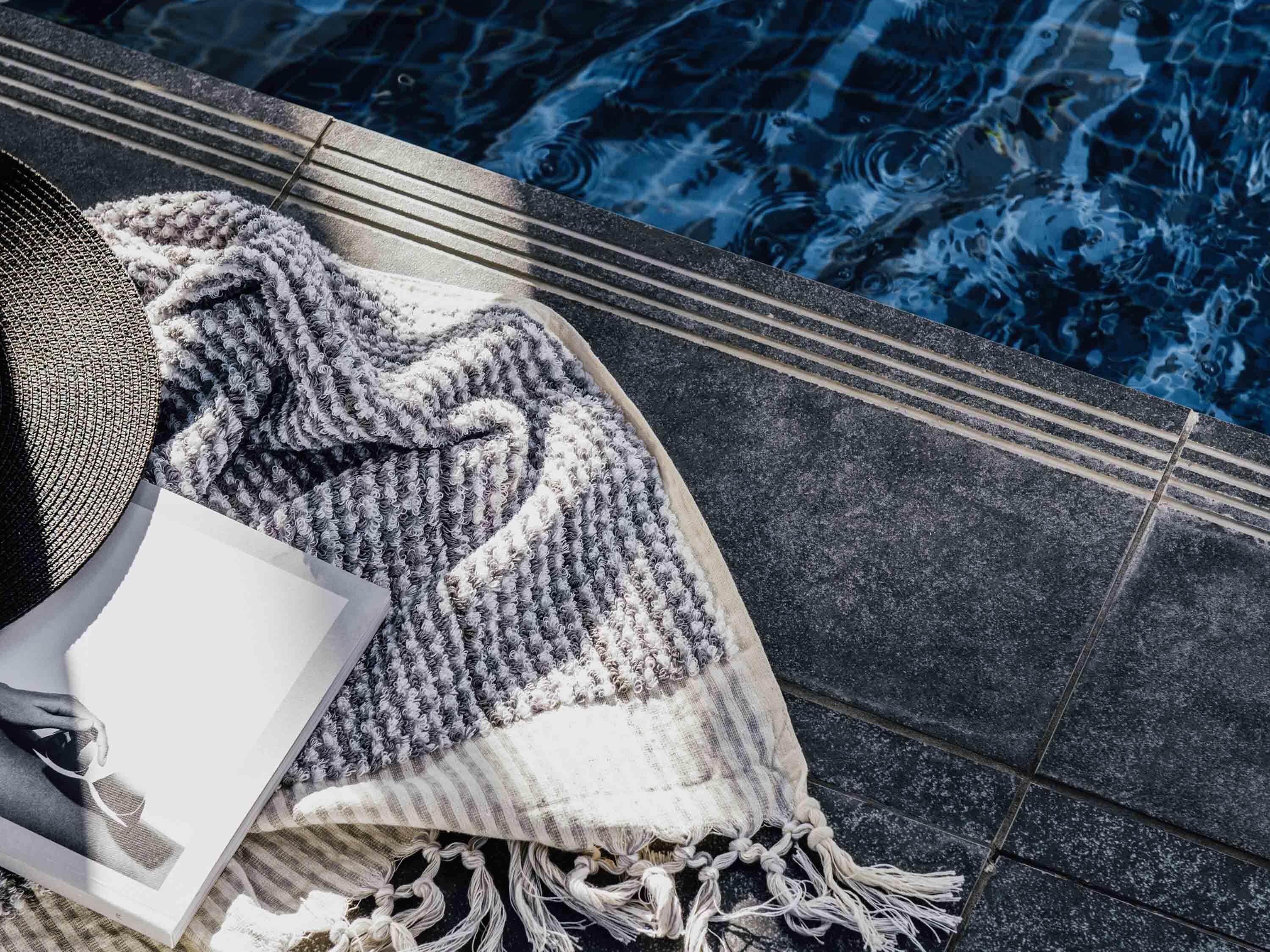 Zona de piscina con una toalla, un libro y una manta.