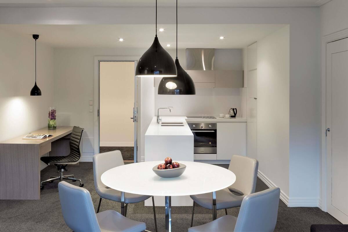 A modern kitchen with white cabinets, a stainless steel range hood, and a built-in oven.