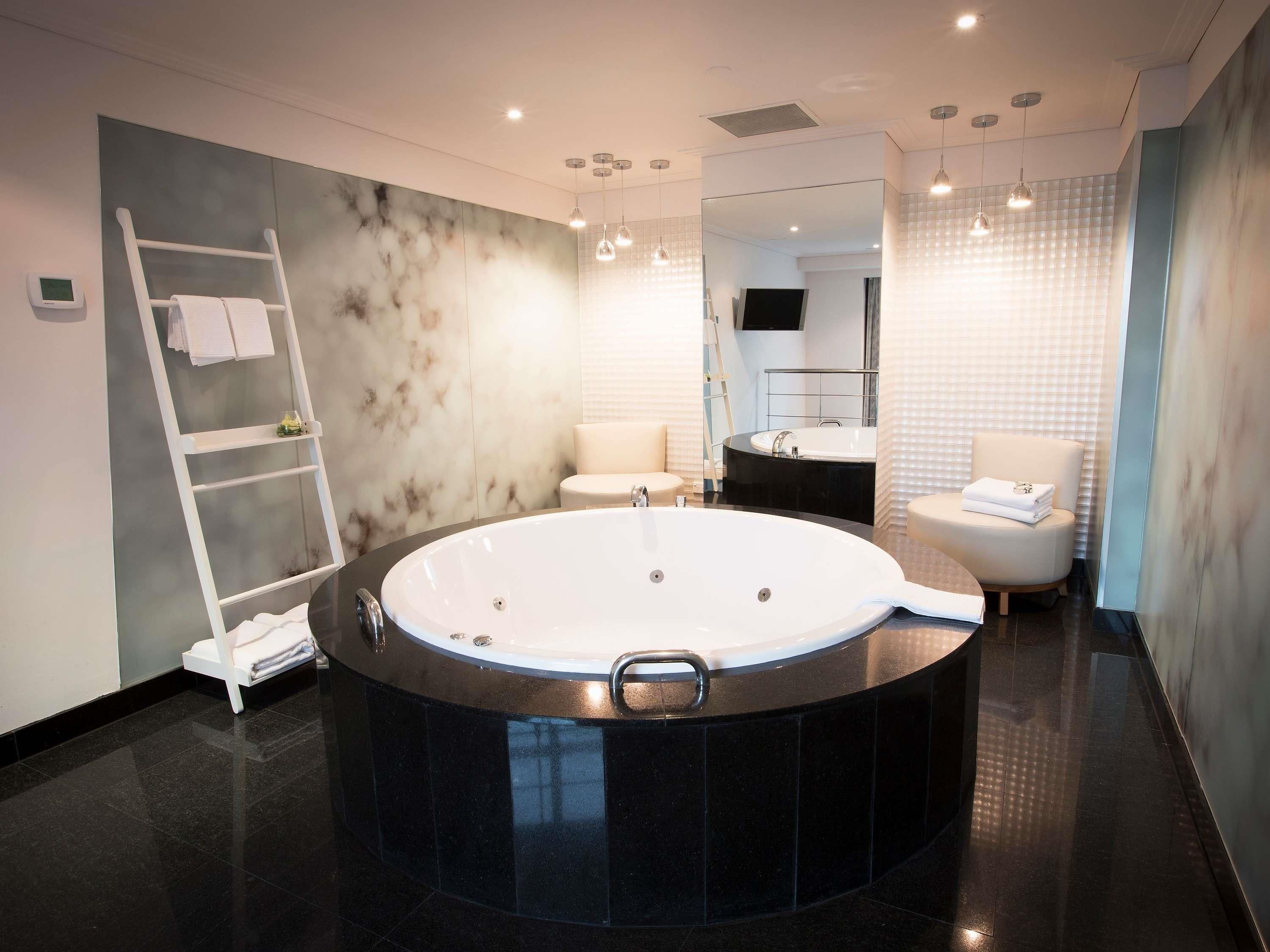 A modern bathroom with a large circular bathtub, a white vanity, a mirror, and a towel rack.