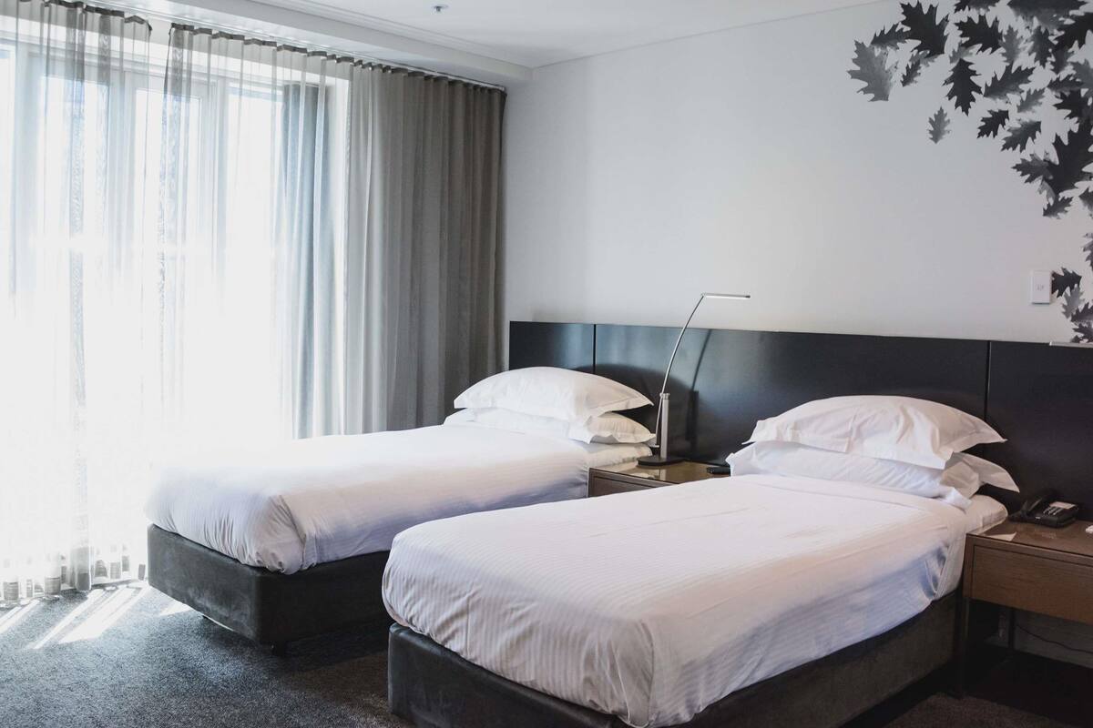 A hotel room with two beds, a nightstand, a lamp, and a wall with a leaf pattern.