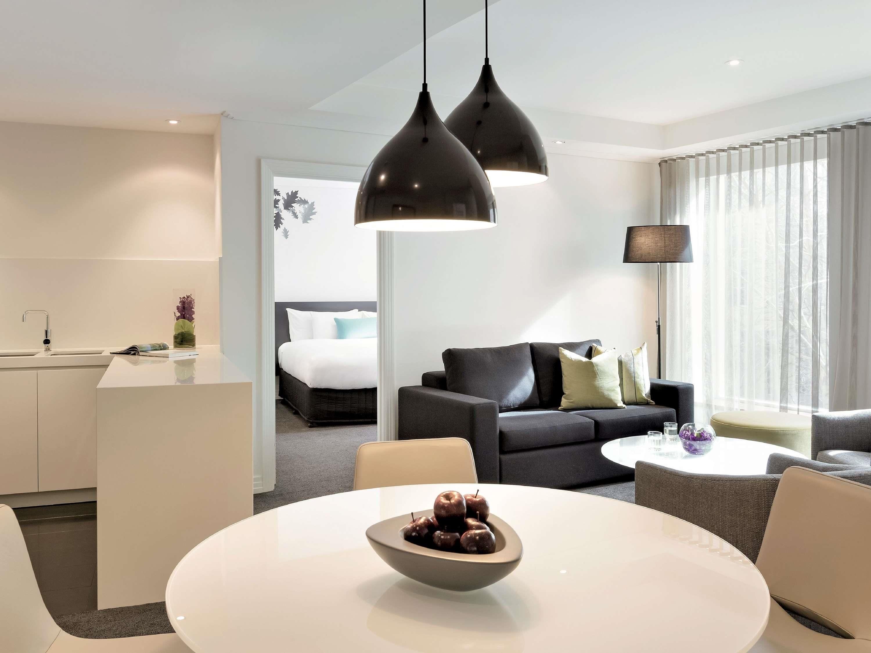 Habitación de hotel moderna con zona de comedor, sofá, cama y vistas al exterior.