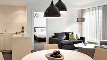 Habitación de hotel moderna con zona de comedor, sofá, cama y vistas al exterior.