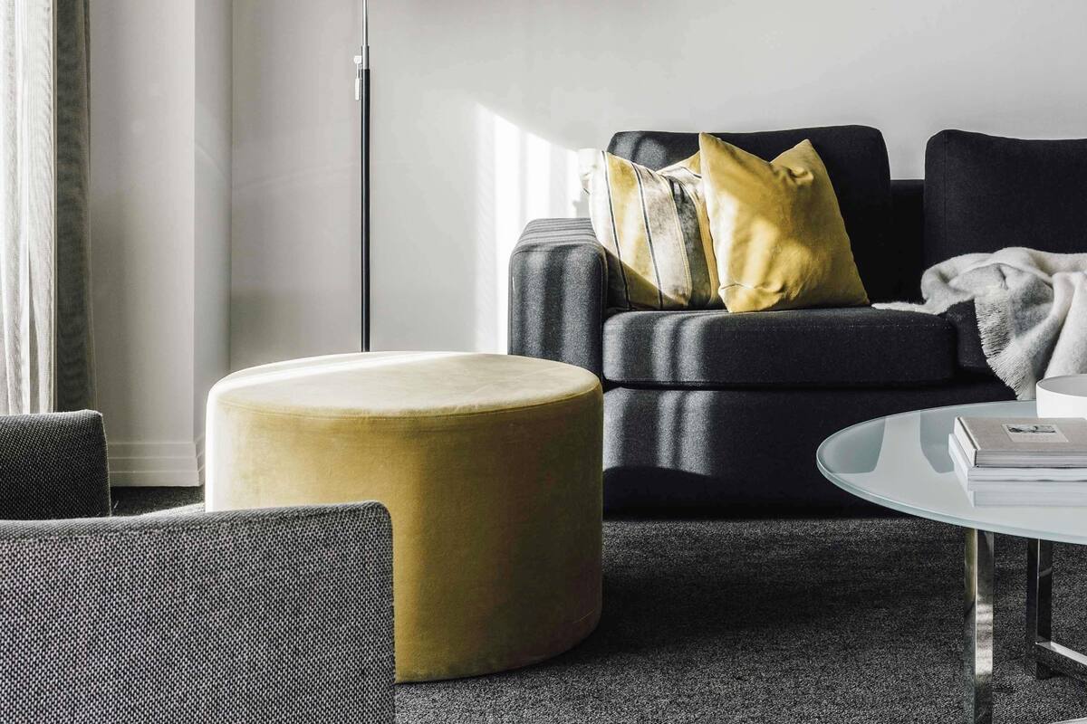 A modern living room with a sofa, ottoman, and a glass coffee table.