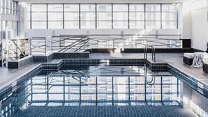 A modern indoor pool with clear glass walls, a tiled floor, and a metal staircase leading to a higher level. - The Como Melbourne by Accor (South Yarra)