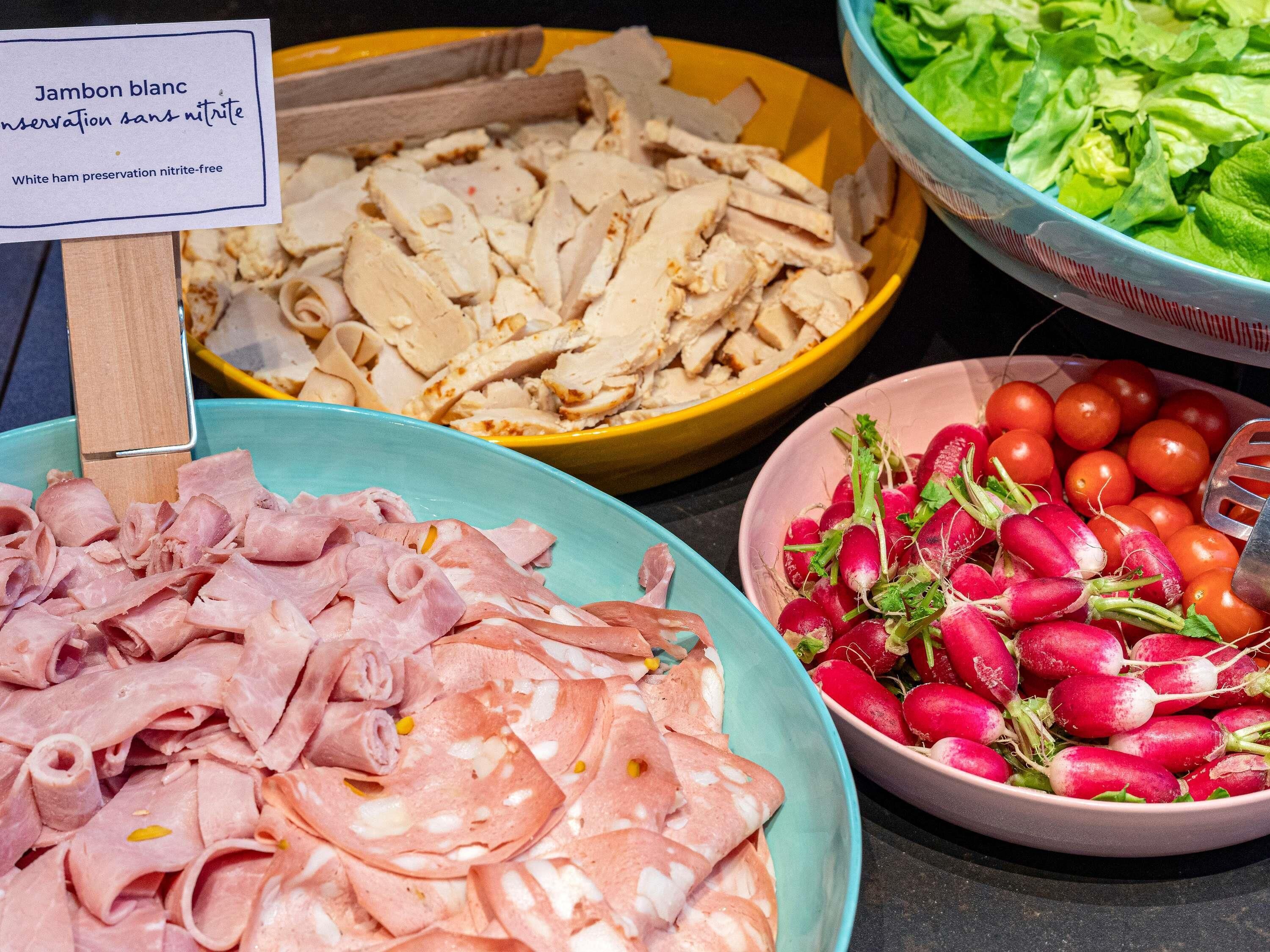 A buffet with various food items including sliced meats, mushrooms, lettuce, radishes, and tomatoes.