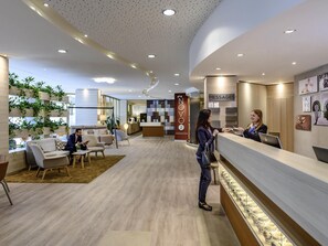 A modern reception area with a counter, seating, and a wall with a 'NOVO 2' sign. - Novotel Frankfurt City (Frankfurt)