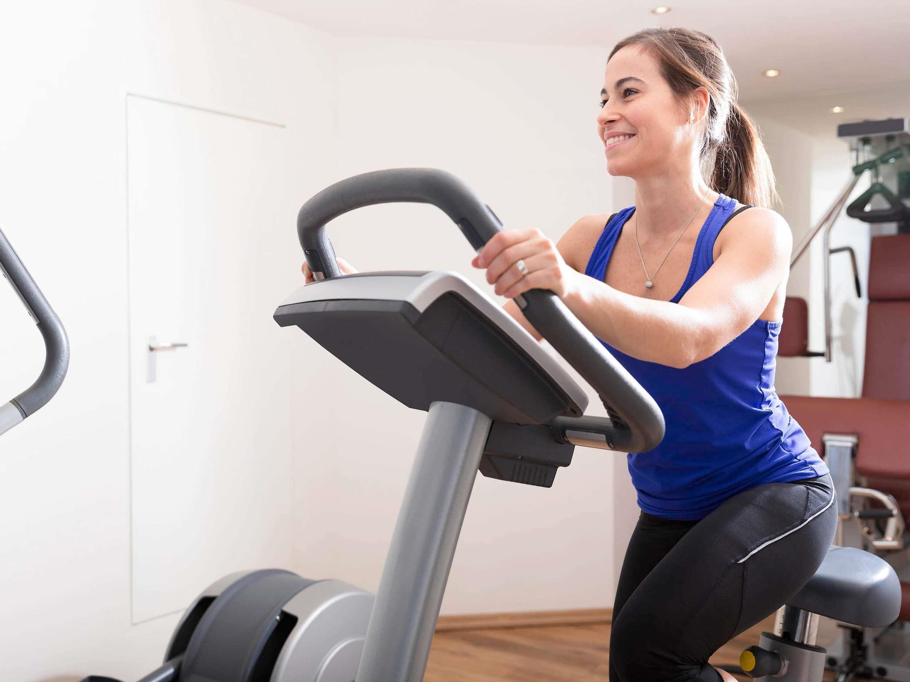 A person using an exercise bike in a room with a door and a staircase in the background.