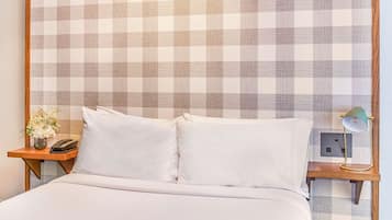 A hotel room with a checkered wall, a bed with white bedding, a bedside table with a lamp, and a phone.