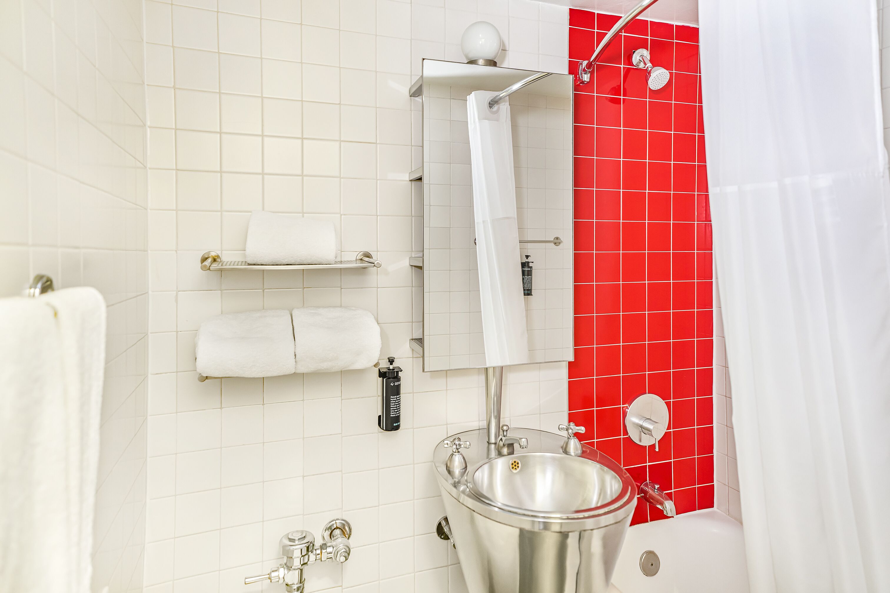 A bathroom with a white sink, a mirror, a shower, and red tiled walls.