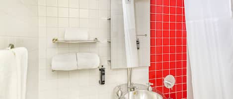 A bathroom with a white sink, a mirror, a shower, and red tiled walls.