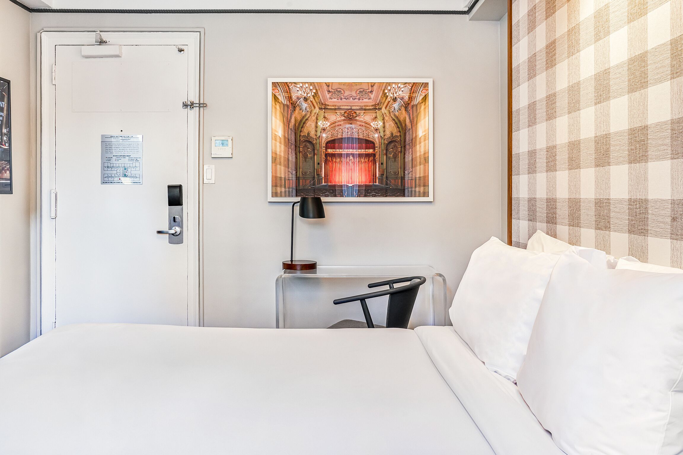 A hotel room with a bed, a desk, and a framed picture of a theater interior.