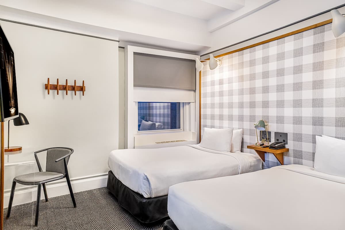 Quarto de hotel com duas camas, uma escrivaninha, uma cadeira e uma janela com vista.