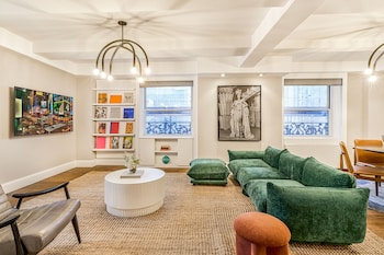 A hotel room with a large bed, a window with a view of buildings, a checkered wall, and a bedside table with a vase of flowers. at Paramount Times Square – A Generator Hotel