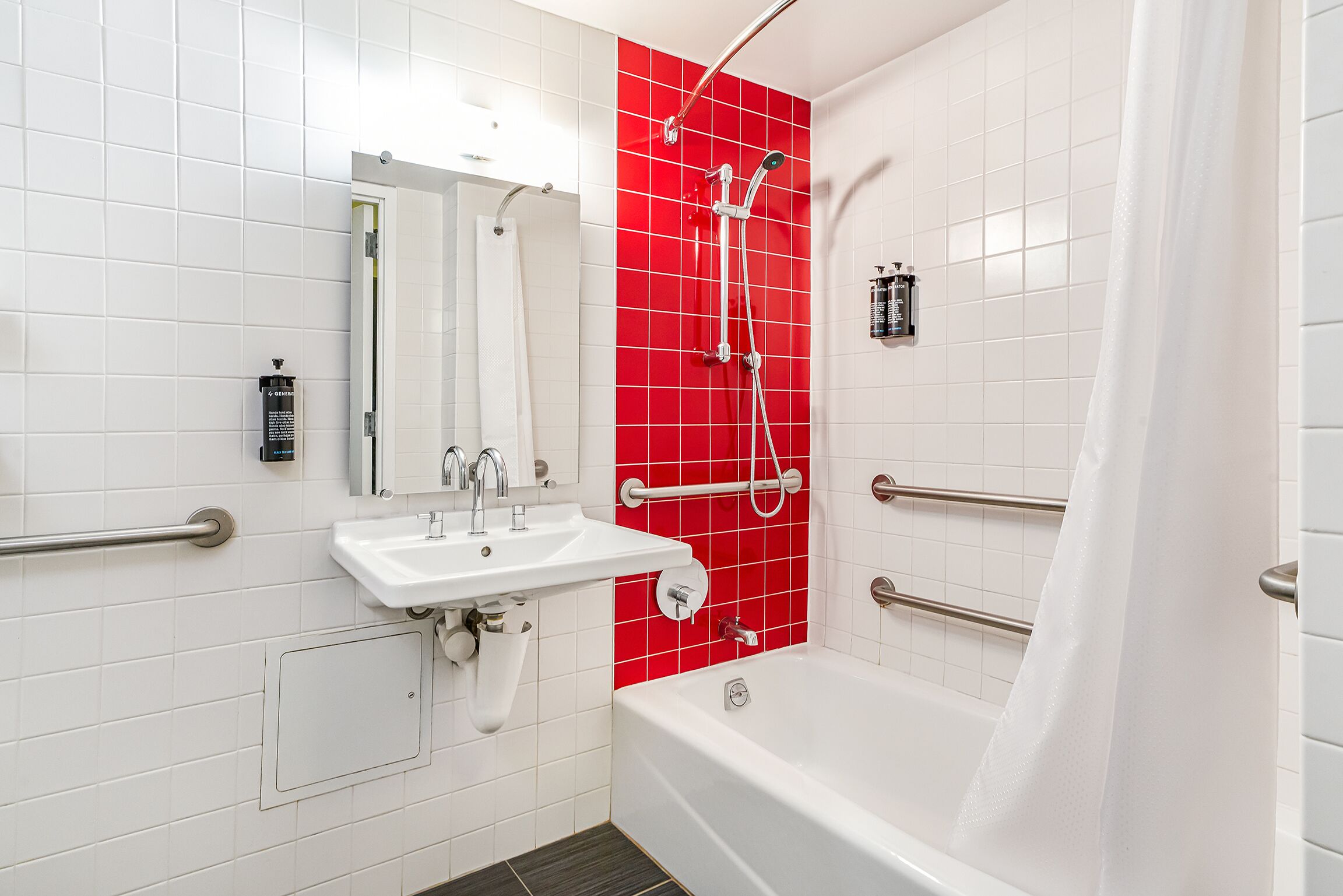 Une salle de bain moderne avec des carreaux blancs, un mur d’accent rouge, une baignoire, un lavabo et une douche équipée de barres d’appui.