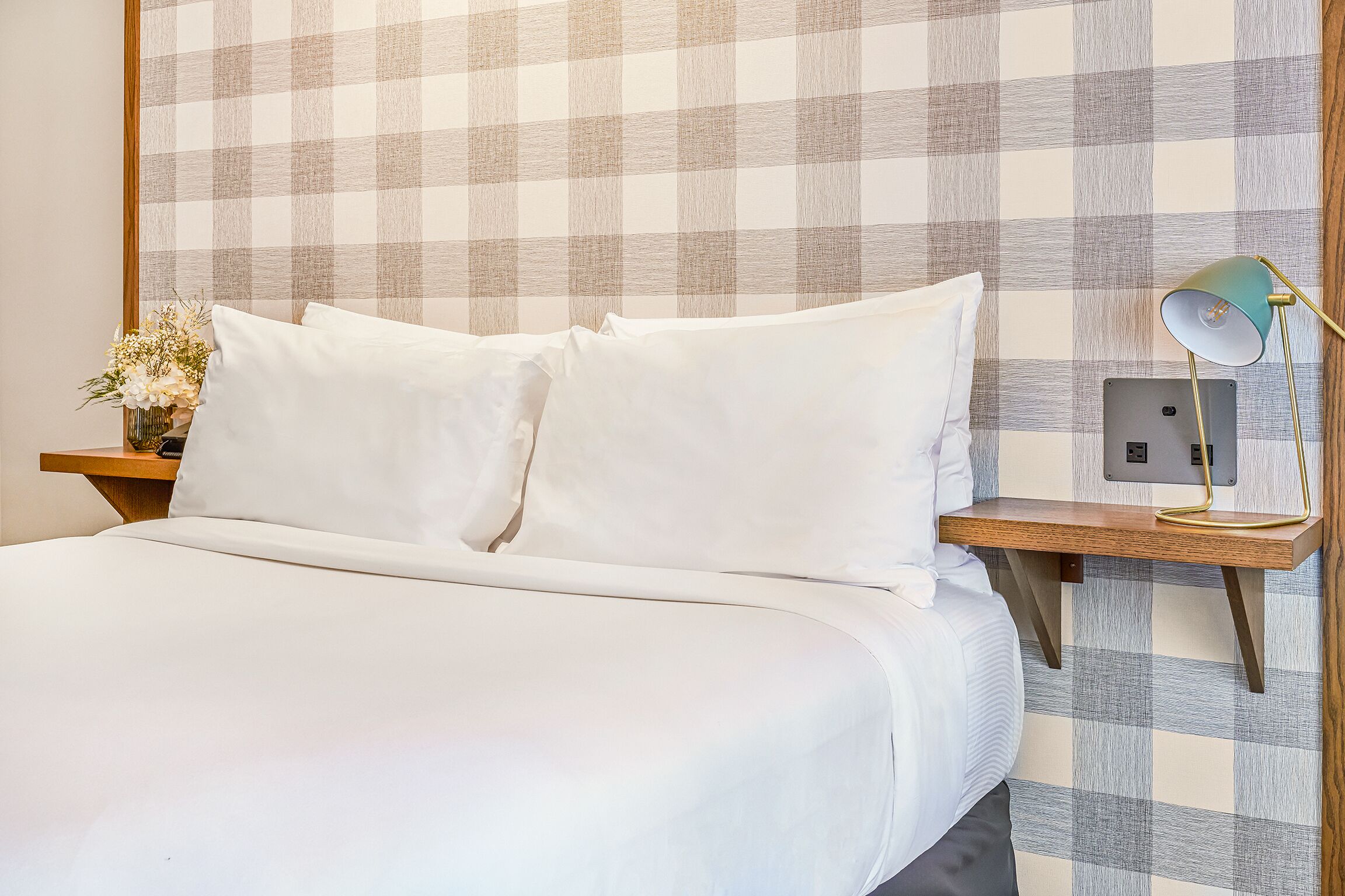 A neatly made bed with white linens, a bedside table with a lamp, and a wall with a checkered pattern.