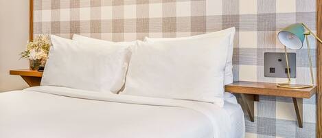 A neatly made bed with white linens, a bedside table with a lamp, and a wall with a checkered pattern.