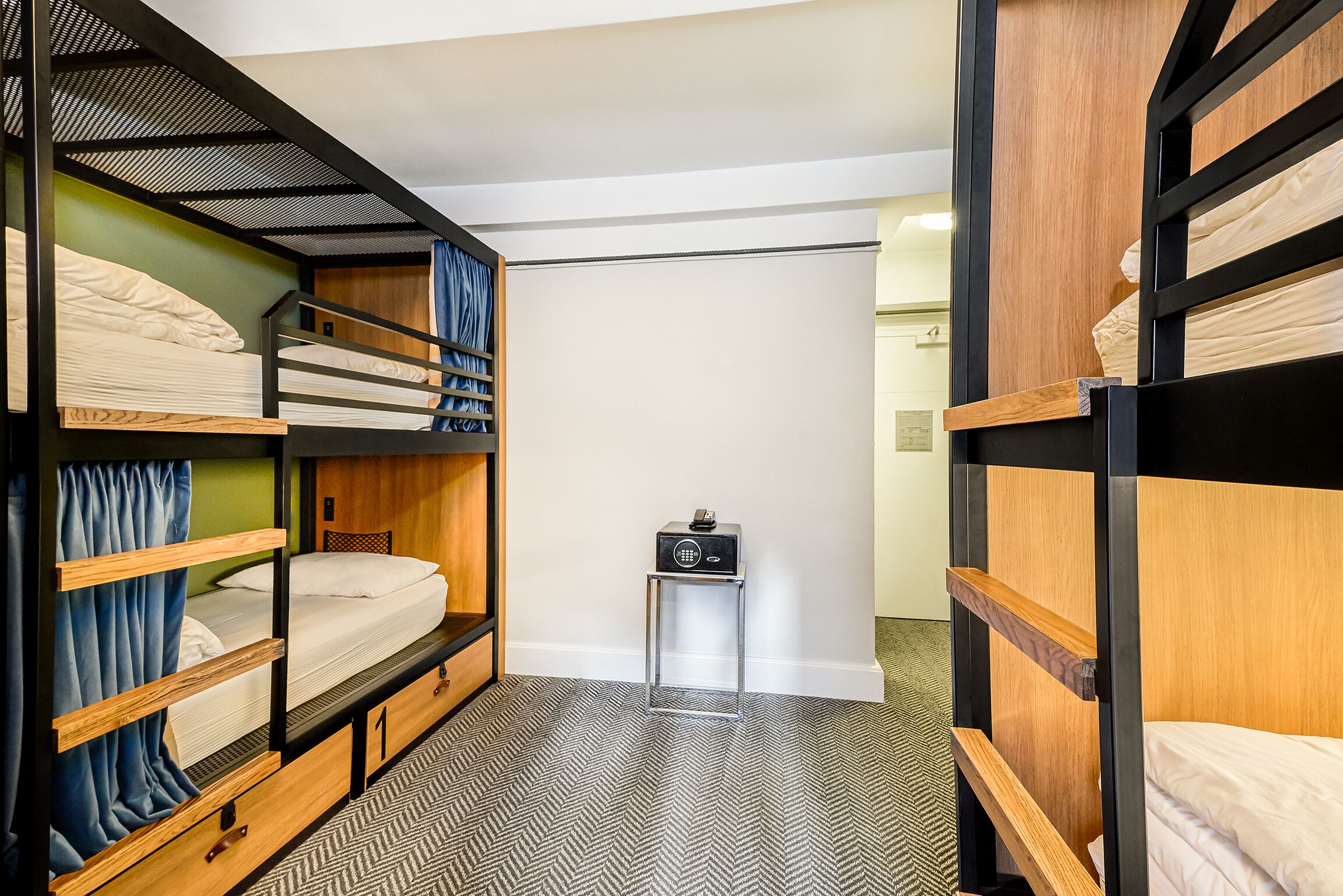 Habitación de hotel compacta con literas, una mesita pequeña y un bote de basura.