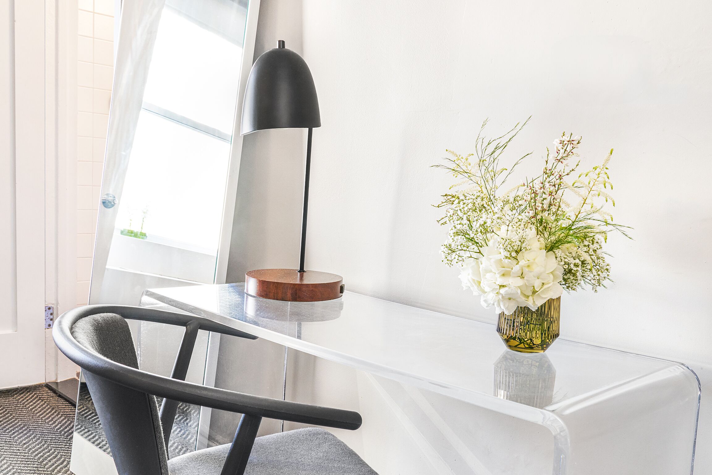 Een modern bureau met een bloevas, een lamp en een stoel in een lichte kamer met een raam.