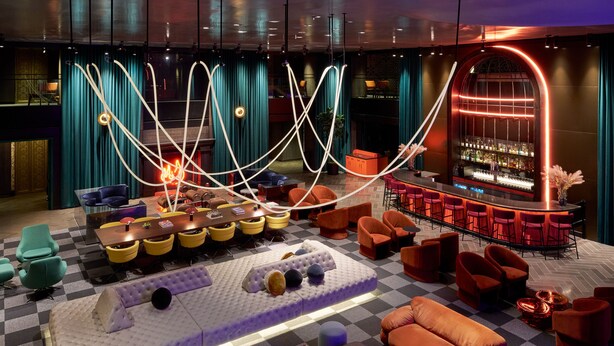 A modern lounge area with a bar, checkered floor, and various seating options including sofas and chairs.