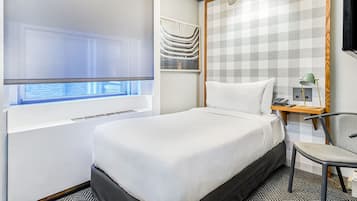 Una habitación de hotel con cama, escritorio con lámpara, silla y ventana con persianas.