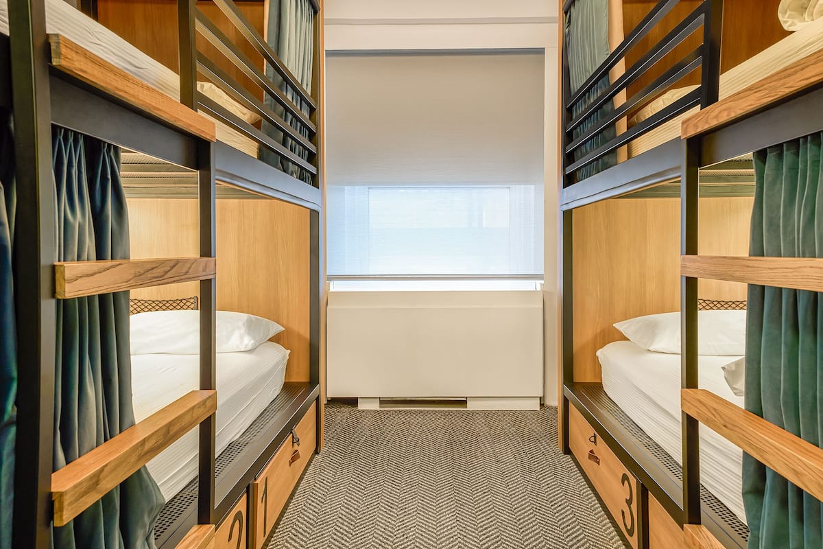 Quarto com beliche, janela, radiador e carpete estampado.