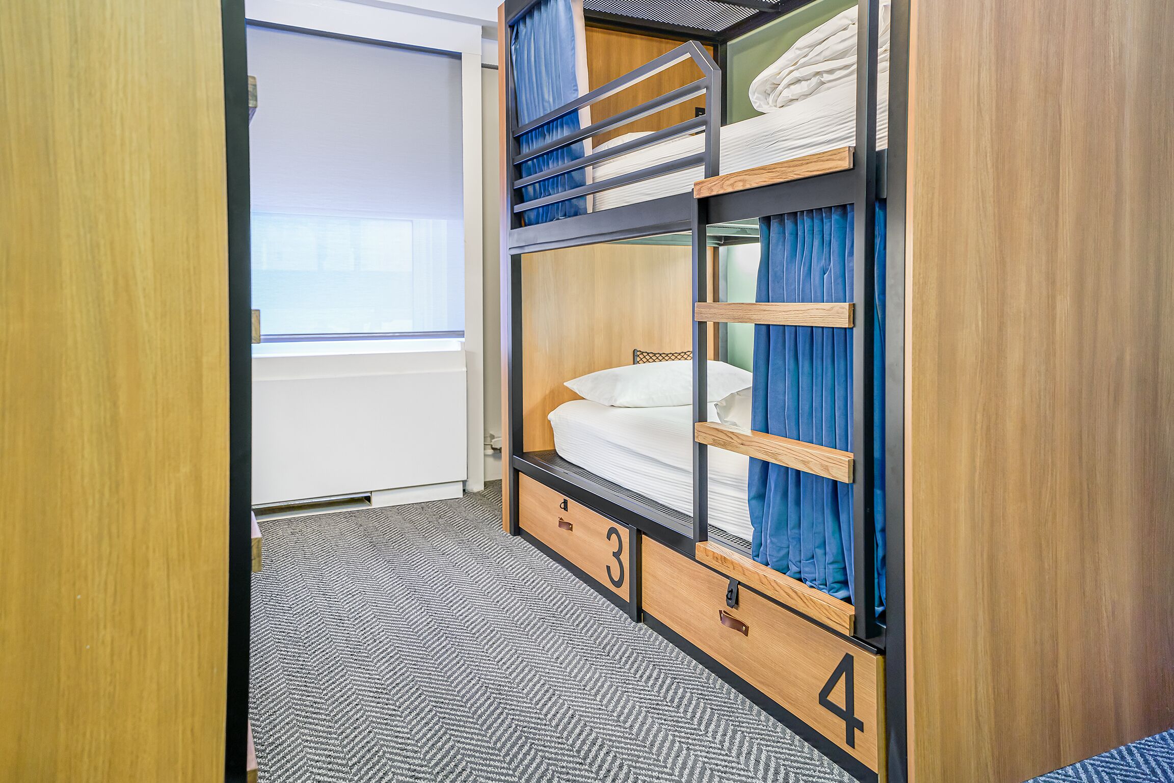 Een slaapkamer met stapelbed, raam, deur en een vloerbedekking.