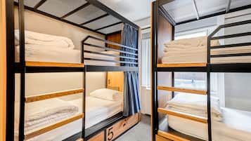 Una habitación con literas, el número '5' en el suelo y una ventana con cortinas.