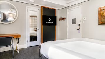A hotel room with a large bed, a desk, a chair, a mirror, a television, and a door.